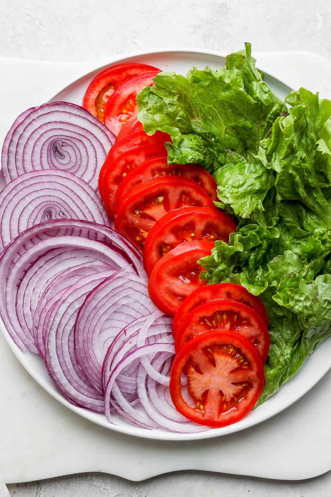 Sliced red onion, tomato, and lettuce on a plate.