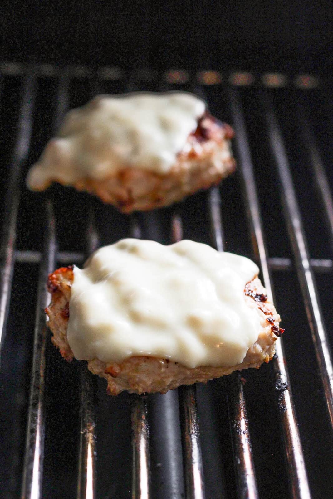 Chicken caesar burgers with cheese on top on the grill.