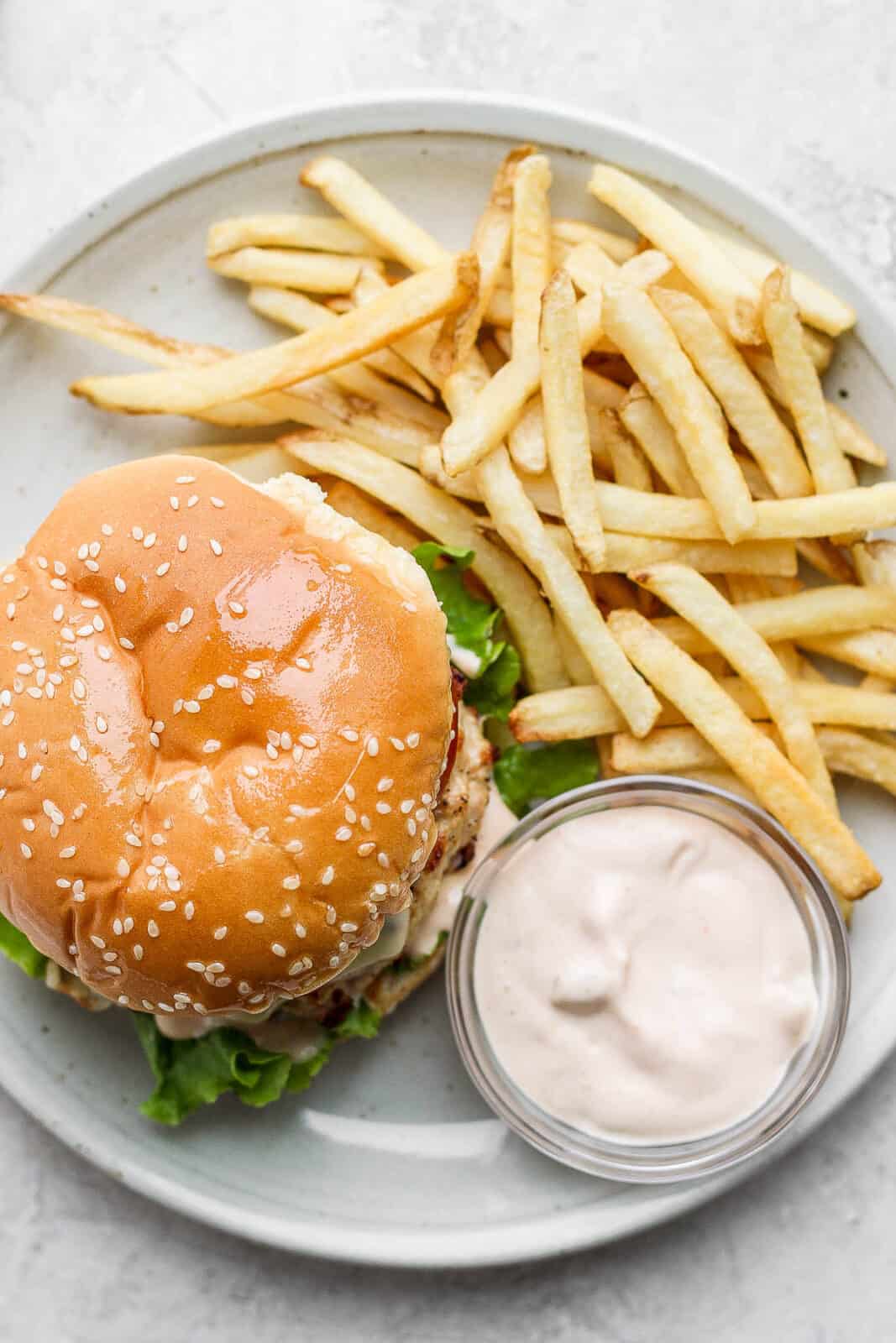 A chicken burger on a plate with french fries and a side of burger sauce.