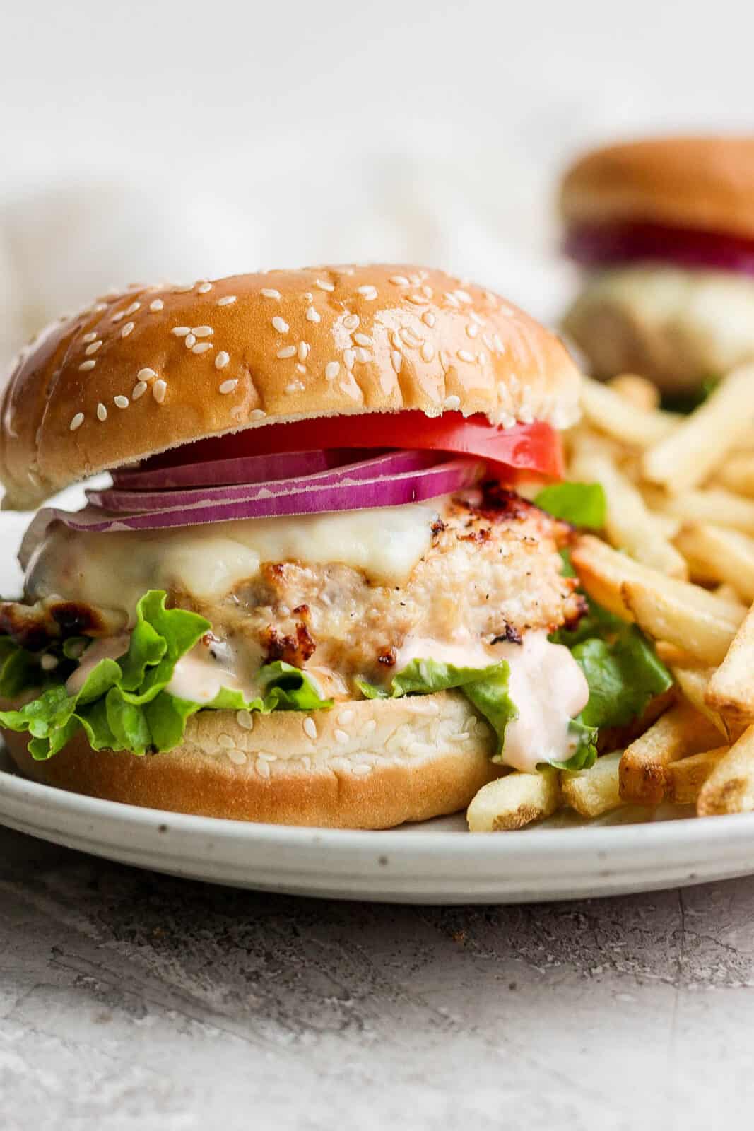 A juicy grilled chicken burger on a plate with french fries.