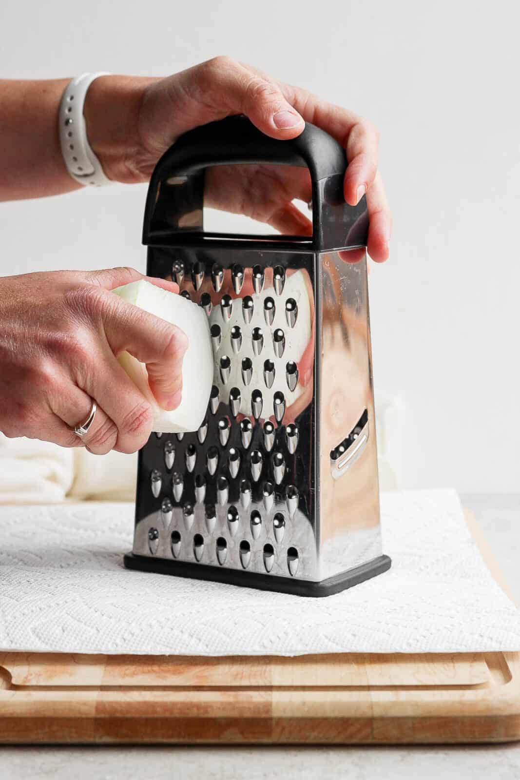 A white onion being grated on a paper towel.