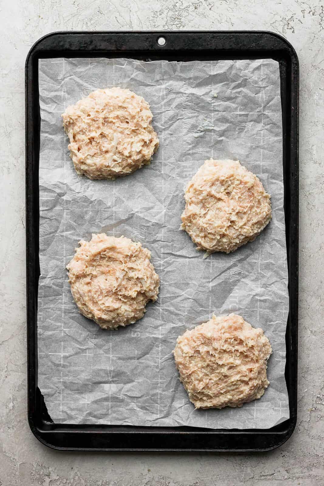 Four chicken patties on a parchment-lined baking sheet.