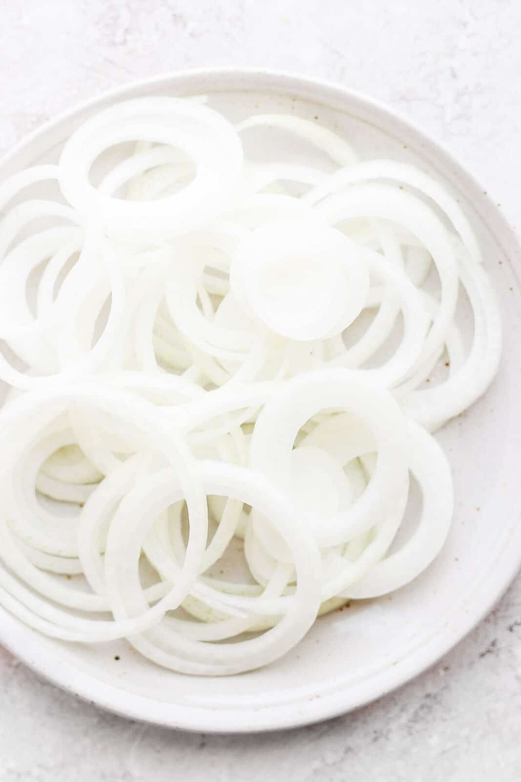Thinly sliced yellow onions on a plate.