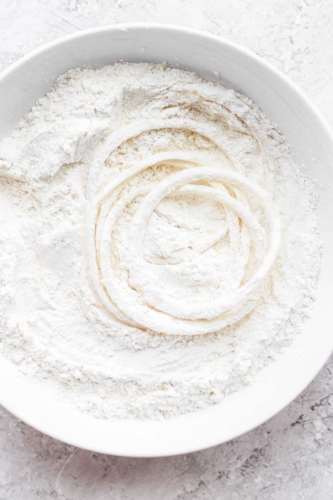 Onion slices in a bowl with flour, salt, onion powder, and garlic powder.