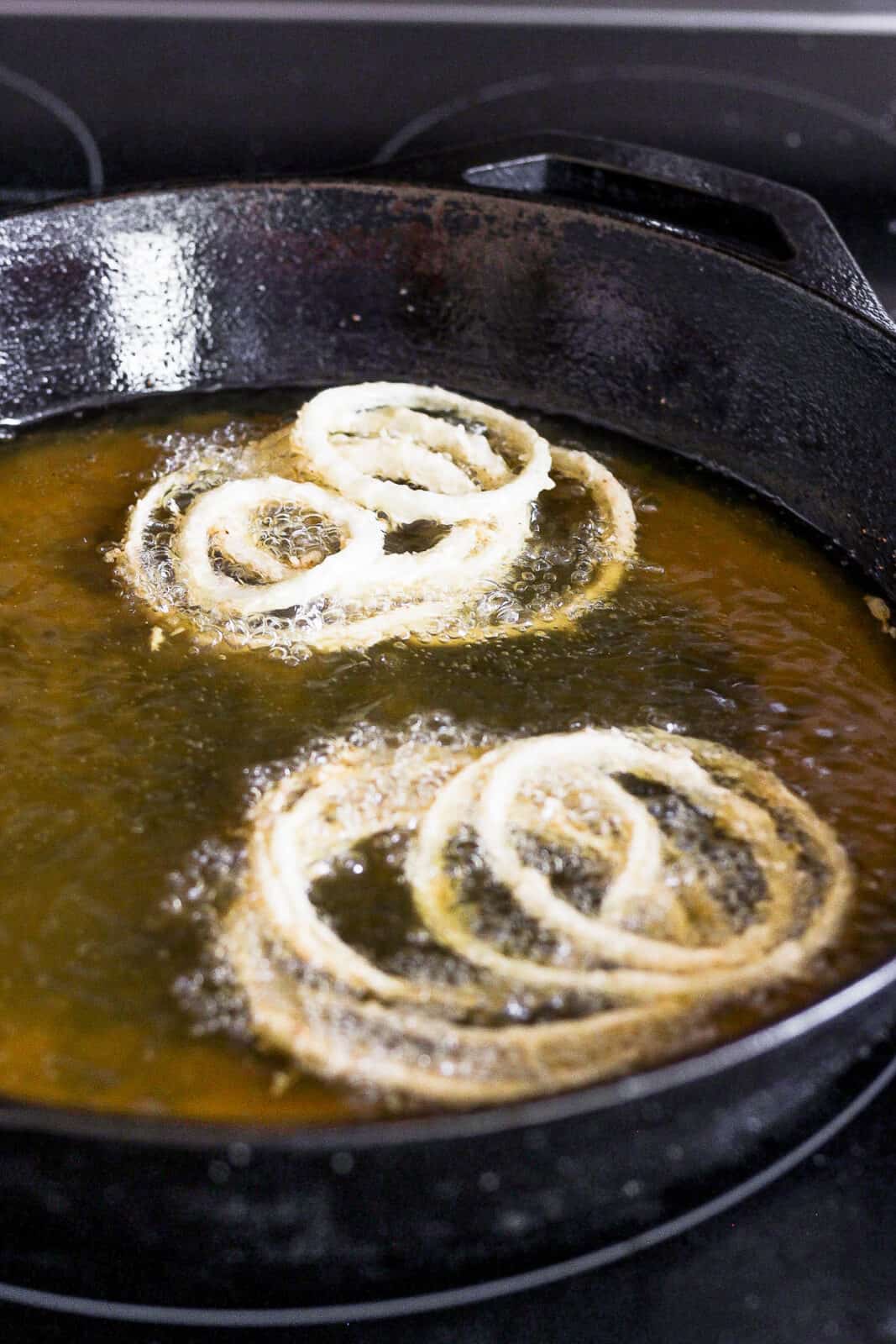 Onion strings frying in avocado oil in a cast iron skillet.