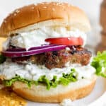 Lamb burger on a bun with tzatziki sauce, onion, lettuce, tomato and feta cheese.