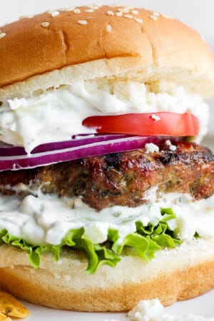 Lamb burger on a bun with tzatziki sauce, onion, lettuce, tomato and feta cheese.