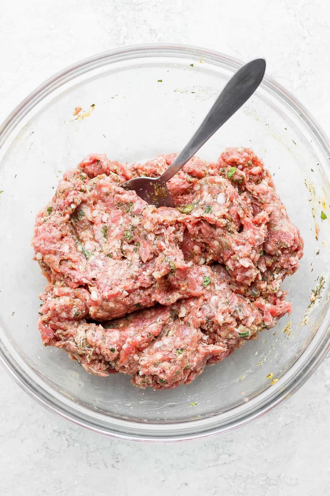 The lamb burger ingredients mixed together in a bowl with a spoon.