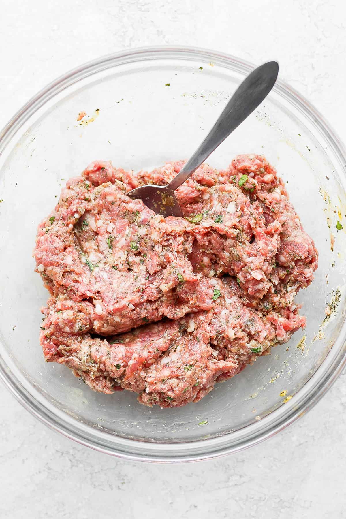 The lamb burger ingredients mixed together in a bowl with a spoon.