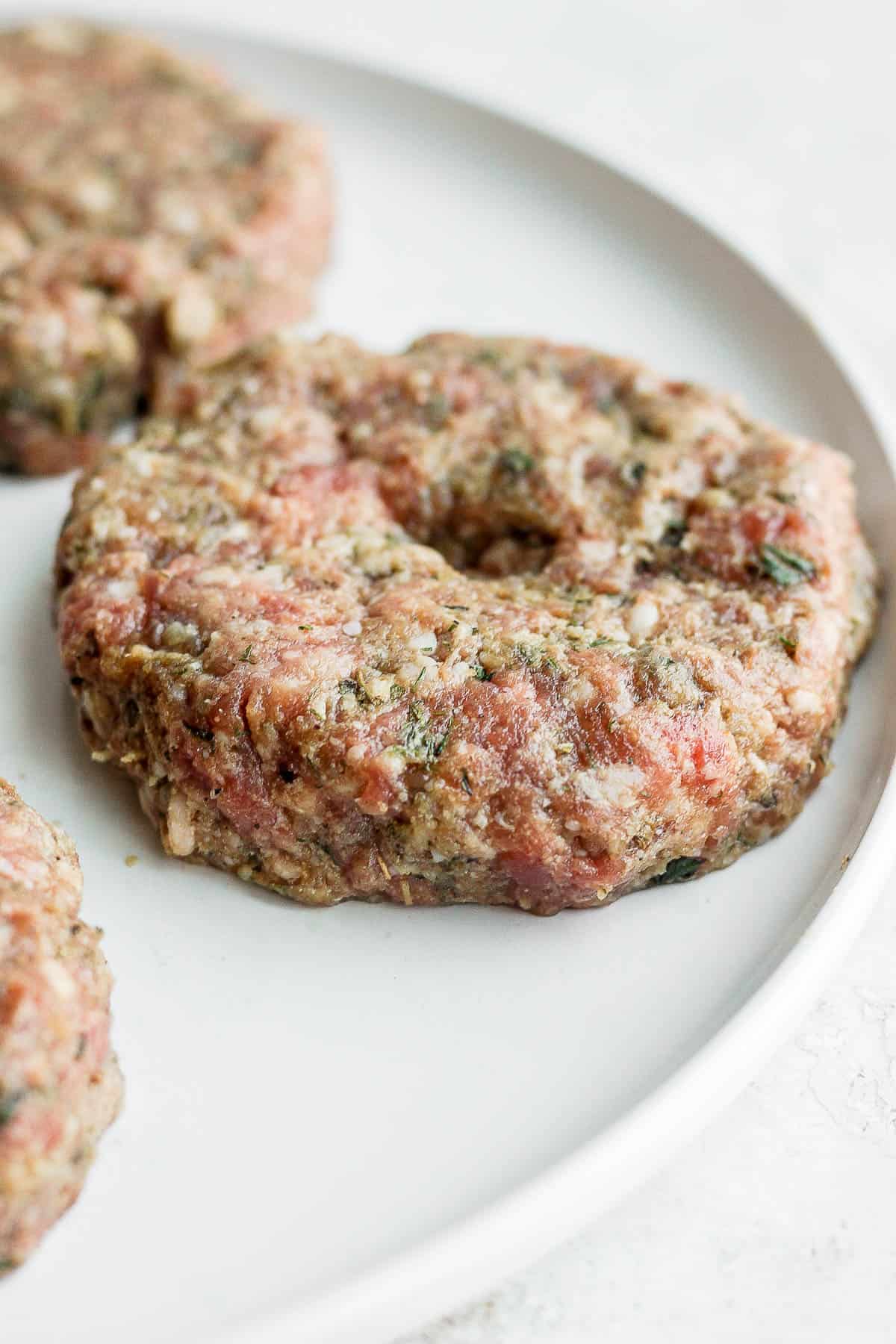 A lamb burger patty on a plate with a thumb indent on top.