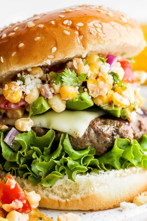 A burger on a bun with lettuce and mexican street corn salad.