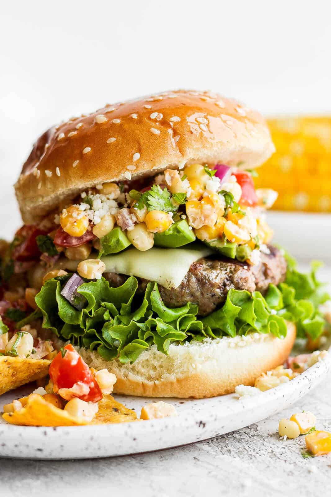 A mexican street corn burger on a plate with fries.
