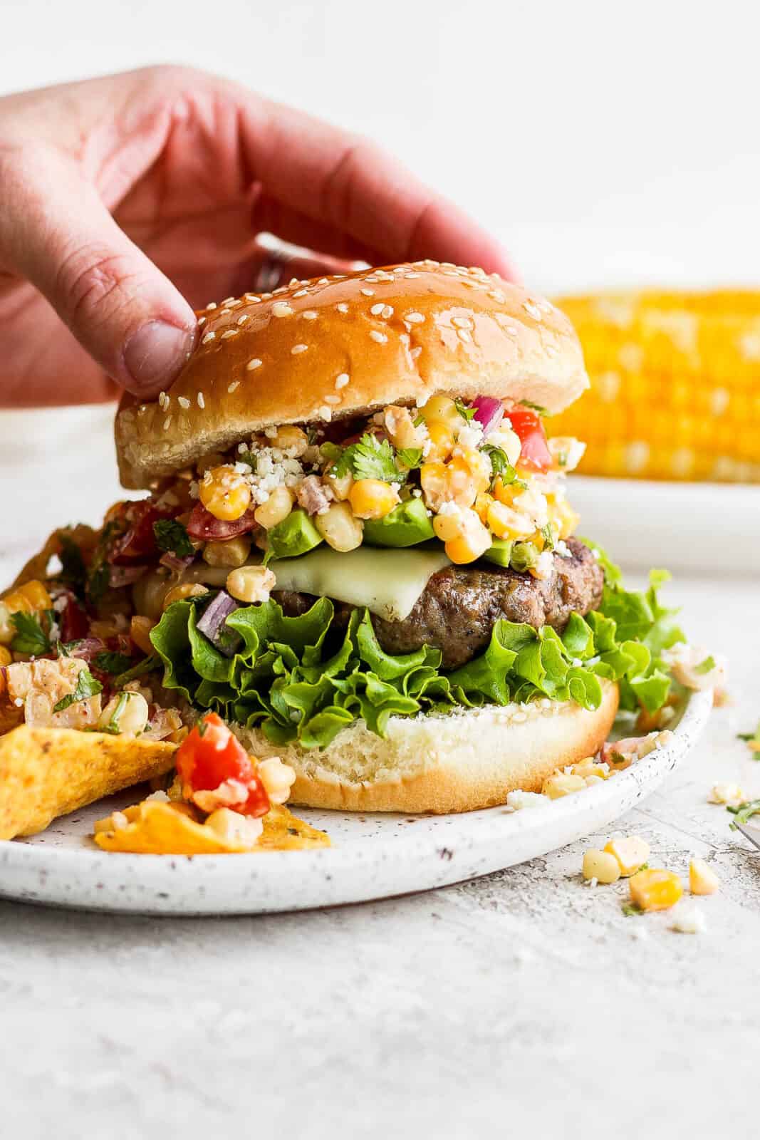 Someone placing the top bun on a mexican street corn burger.