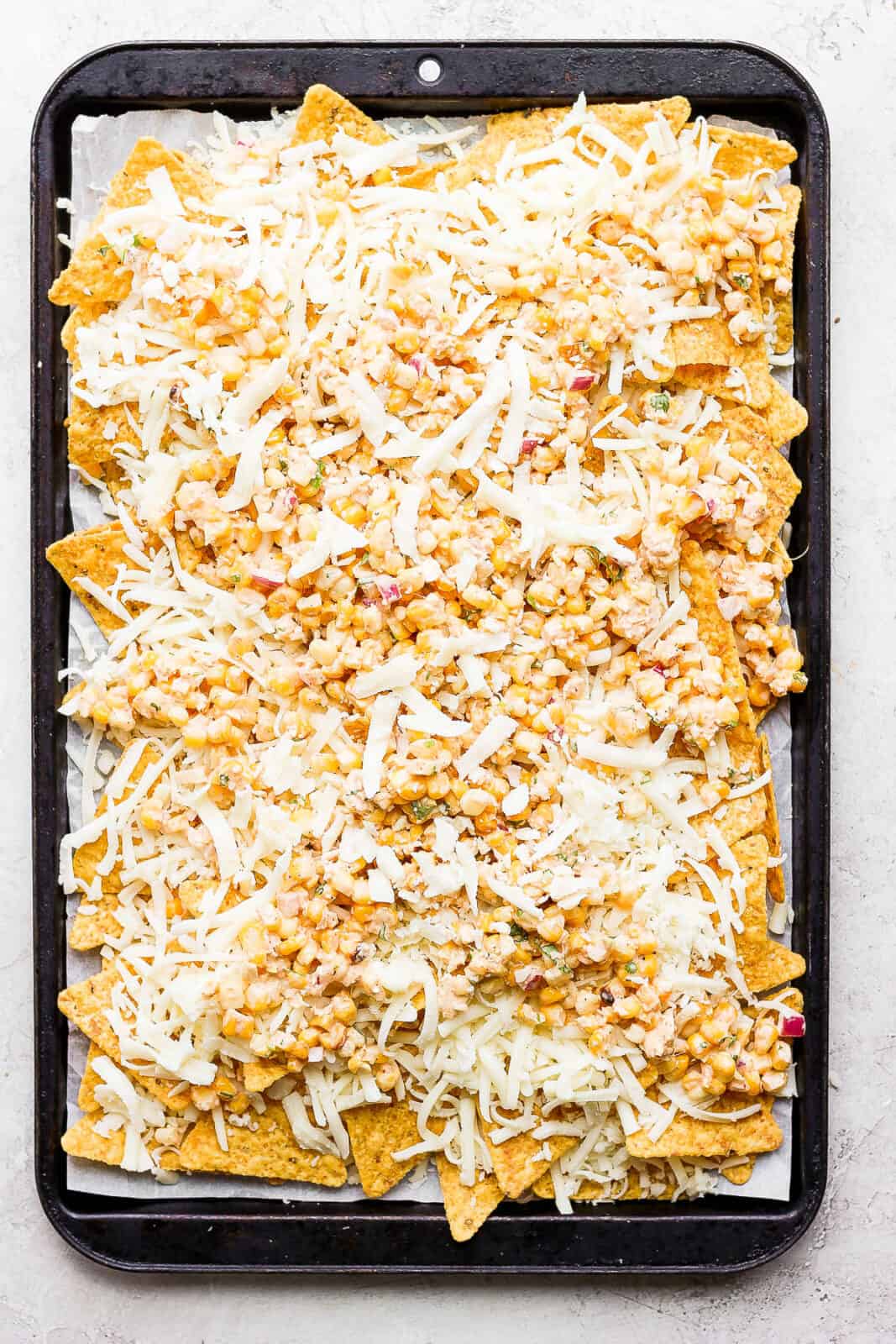 Mexican street corn nachos on a parchment-lined baking sheet before going in the oven.