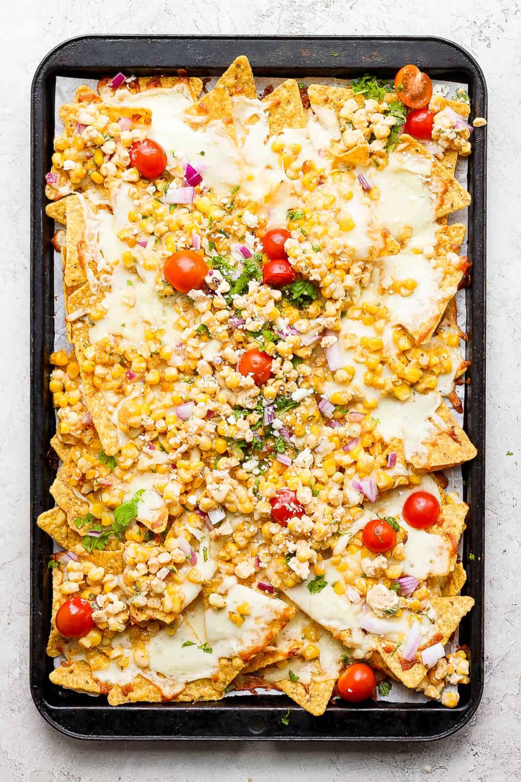 Mexican street corn salad nachos after baking and with fresh toppings on top.