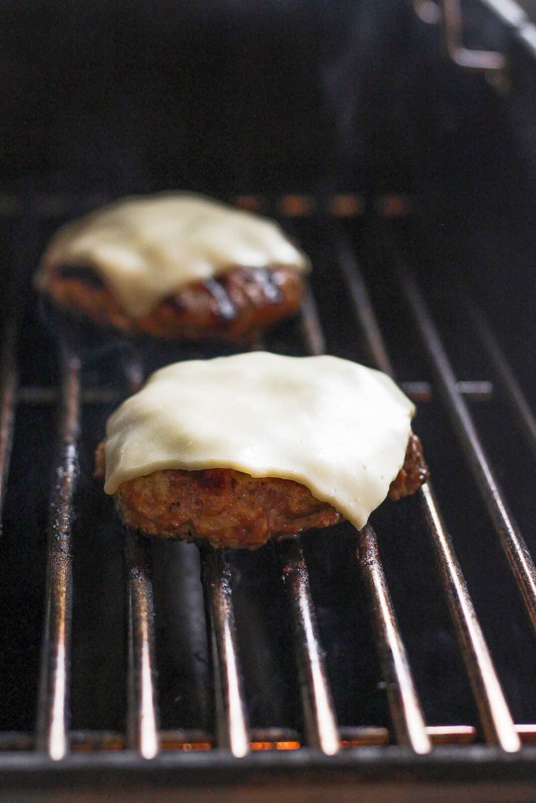 Turkey burgers on the grill with cheese on top.