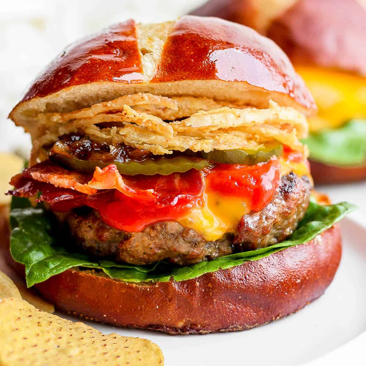 A grilled burger on a pretzel bun with lettuce, ketchup, bacon, pickles and fried onions.