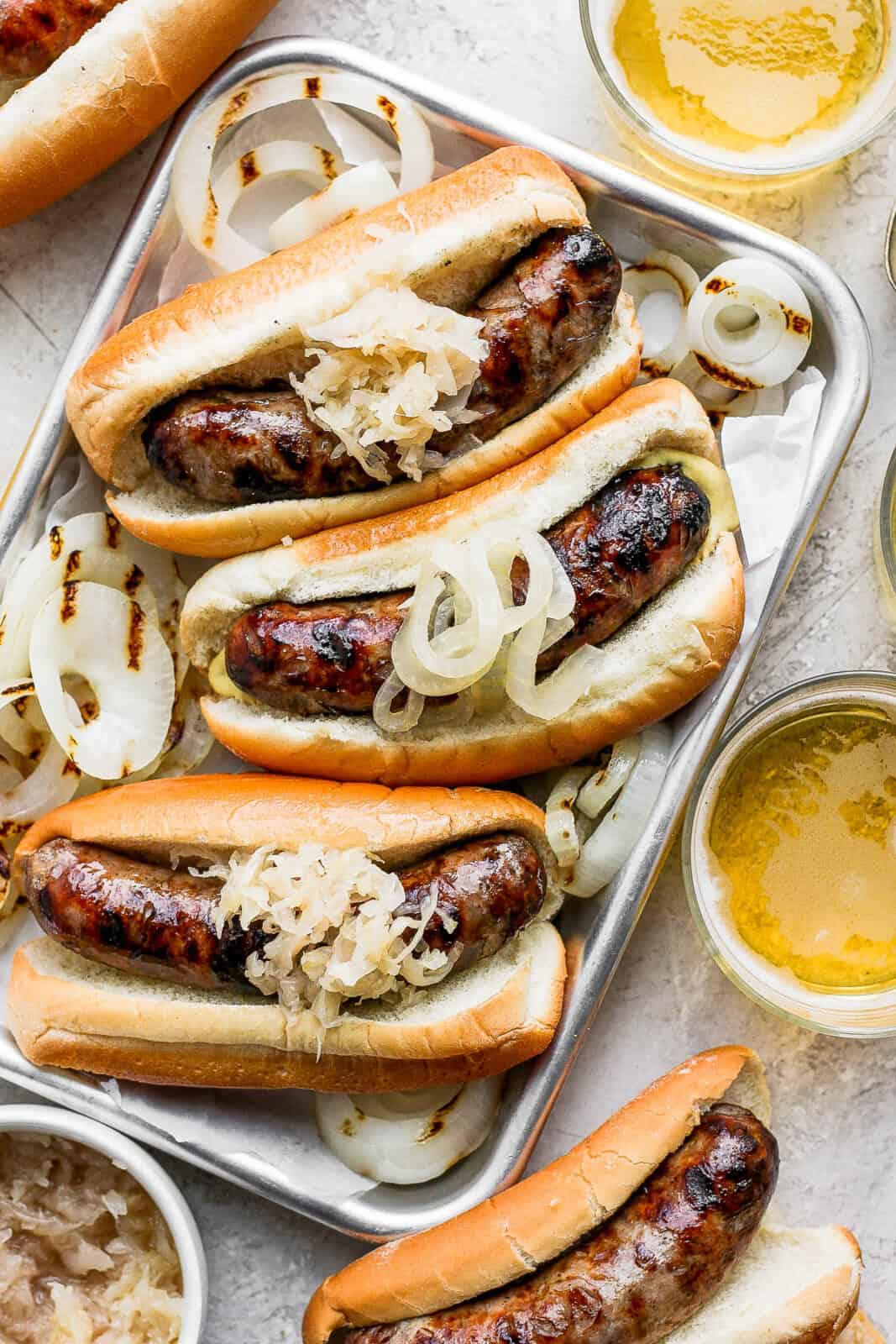 A tray of beer brats with grilled onions and sauerkraut on top.