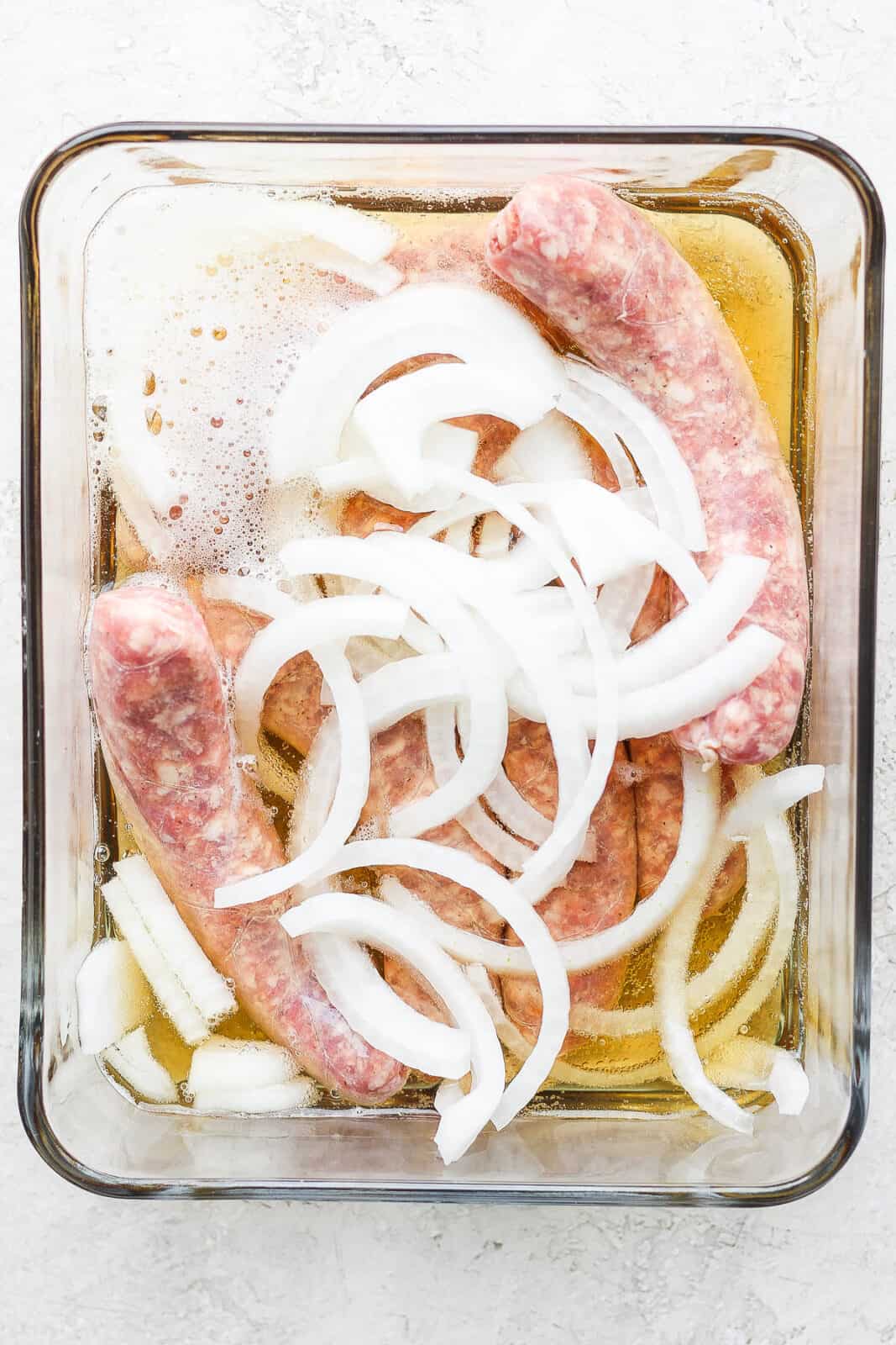 Uncooked brats marinating in beer, onions, and garlic.