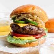 A beer burger on a bun with cheese, onions and jalapeno.
