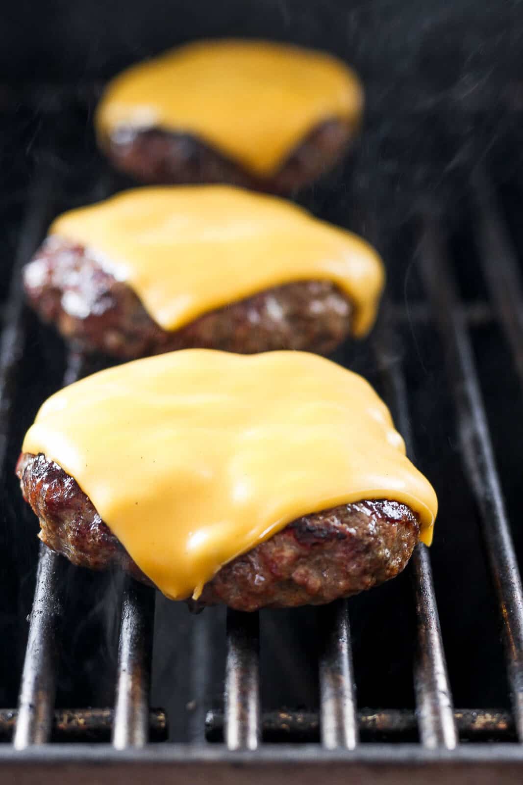 Three burgers on the grill with melted cheese on top. 