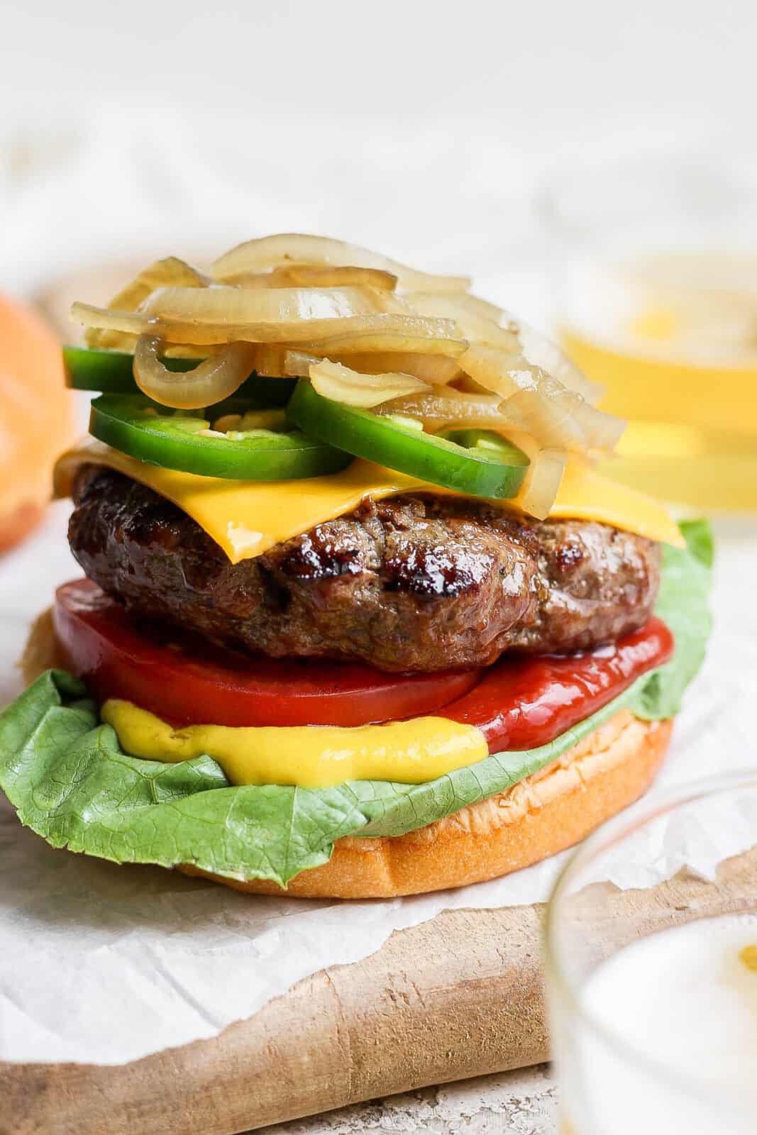 A beer burger on a bottom bun with onions and tomato.