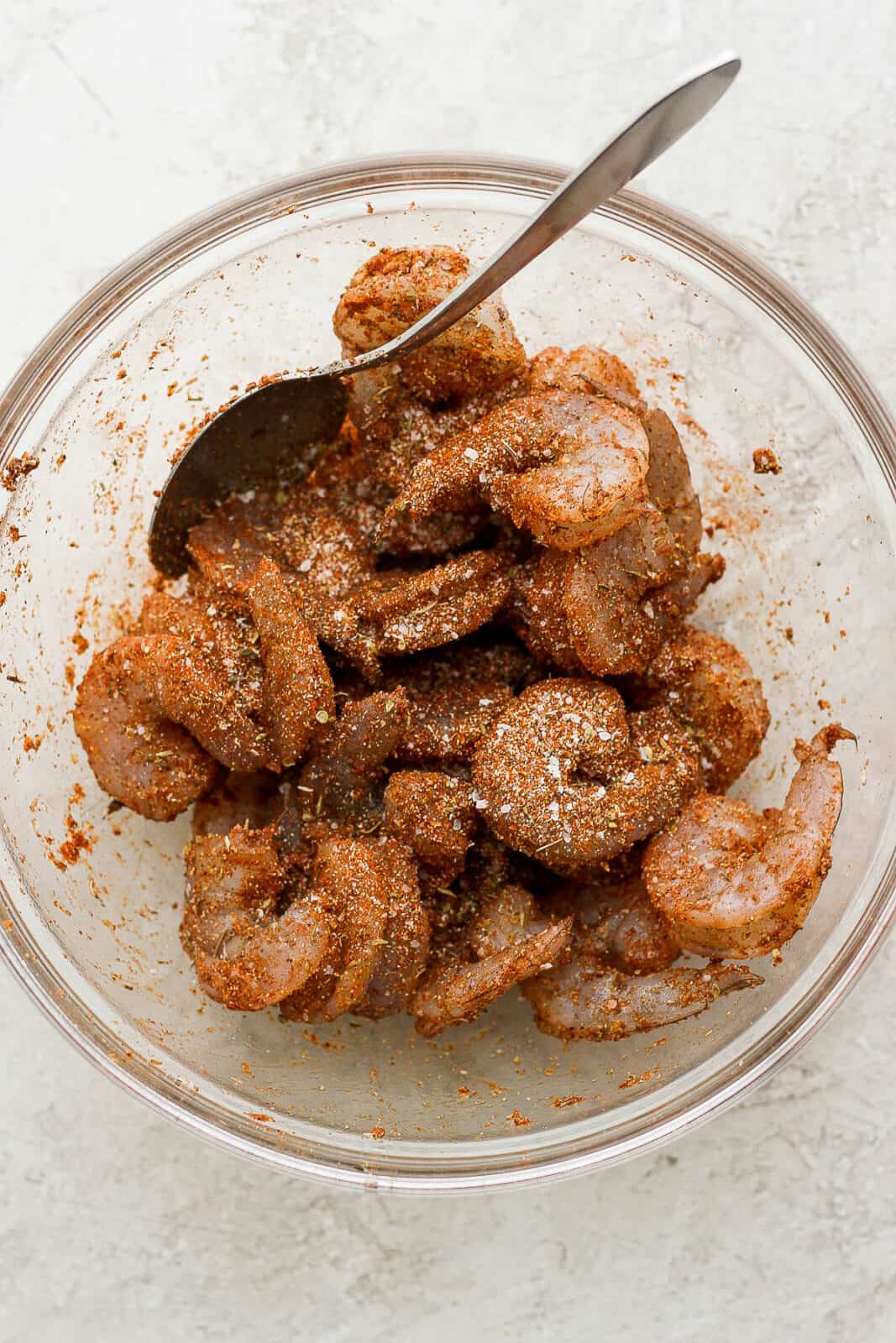 Shrimp being coated with blackened seasoning in a bowl with a spoon.
