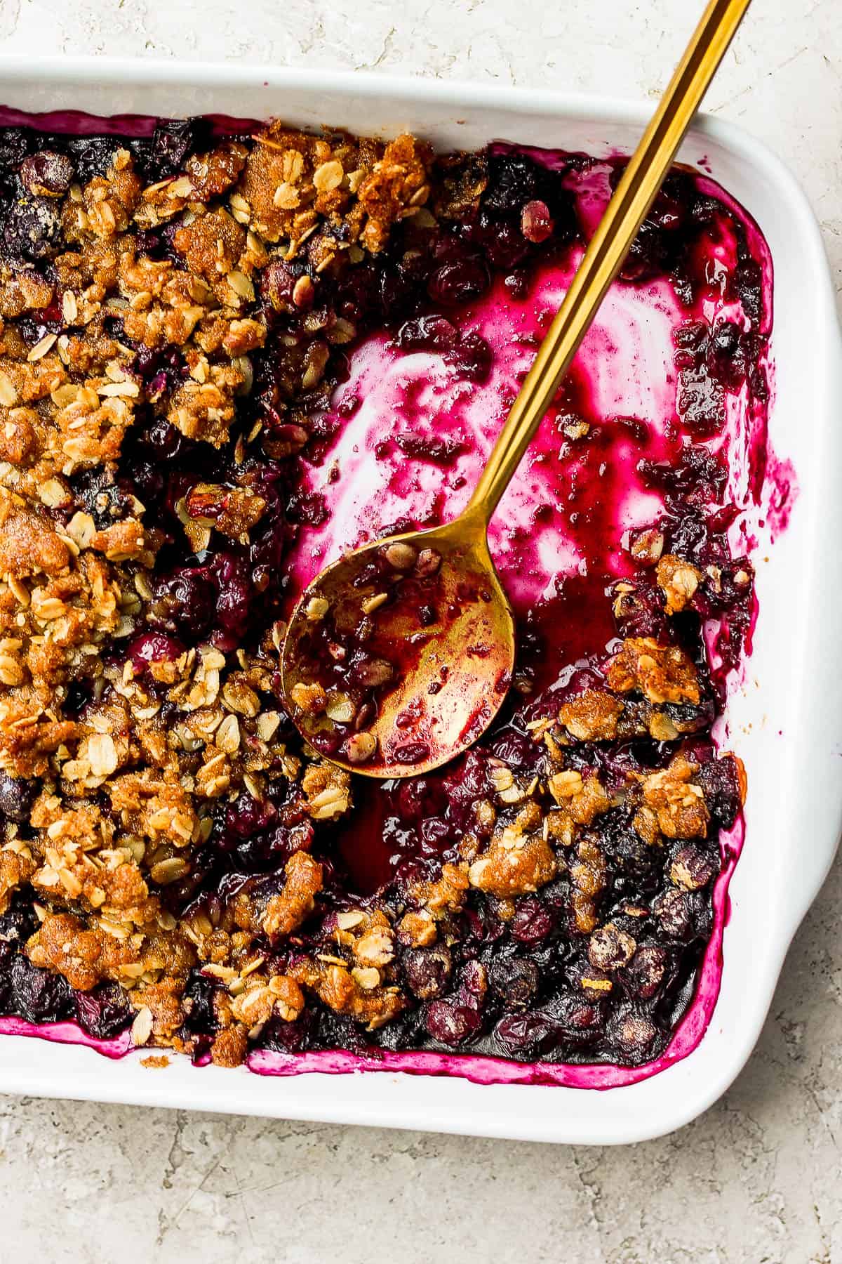 Some of the blueberry crisp removed from the baking dish and a spoon in its place.