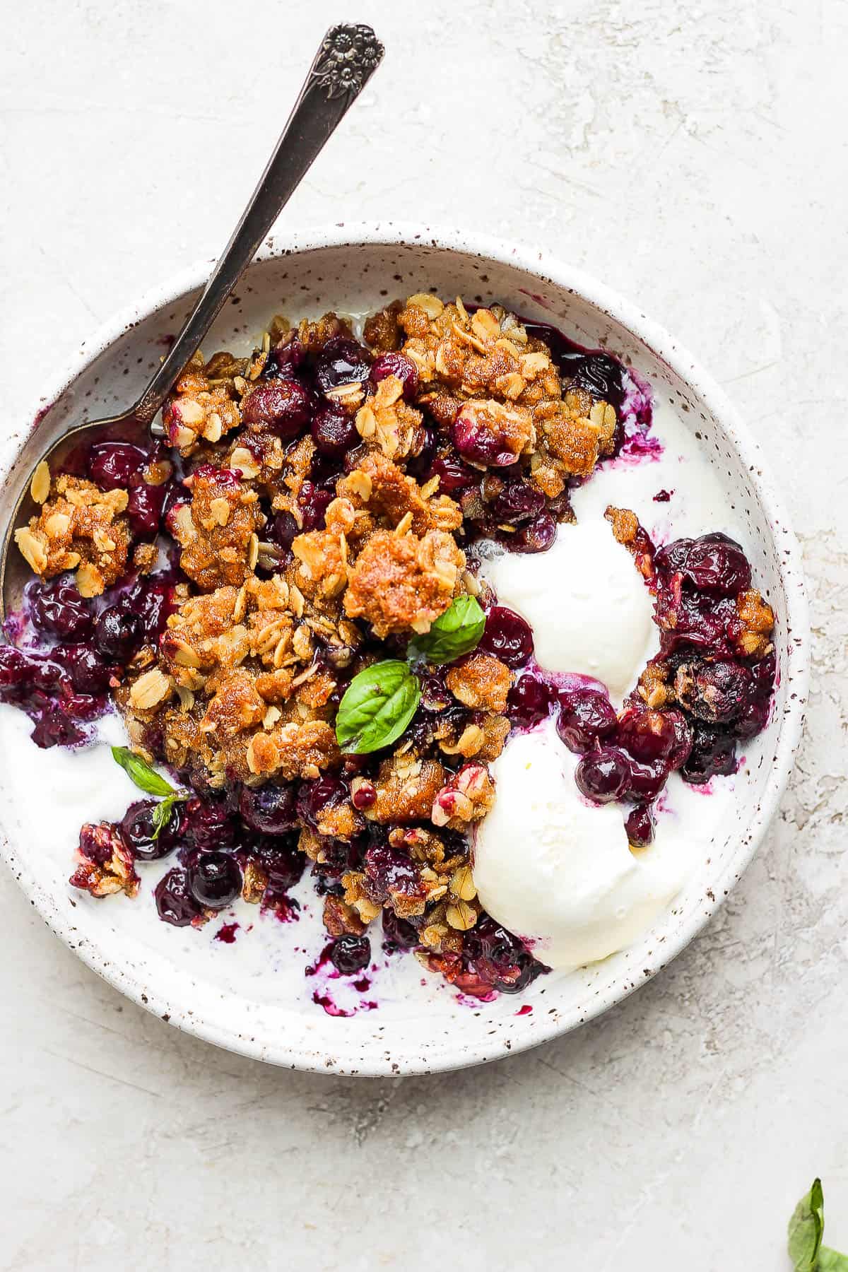 Blueberry crips in a small dish with ice cream and a spoon.