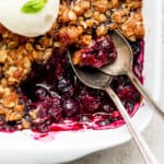 Close up shot of the corner section of 9x9 pan of blueberry crisp with two spoons sticking out.