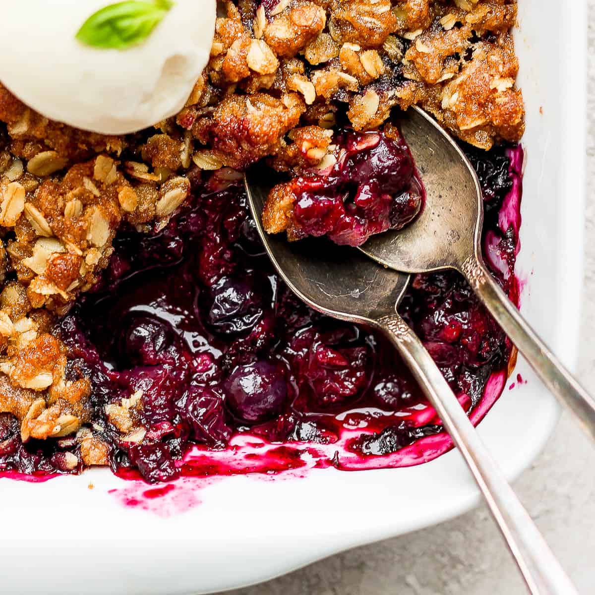 Close up shot of the corner section of 9x9 pan of blueberry crisp with two spoons sticking out.