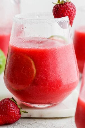 A strawberry margarita in a glass with a lime inside and fresh strawberry for garnish.