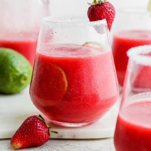A strawberry margarita in a glass with a lime inside and fresh strawberry for garnish.