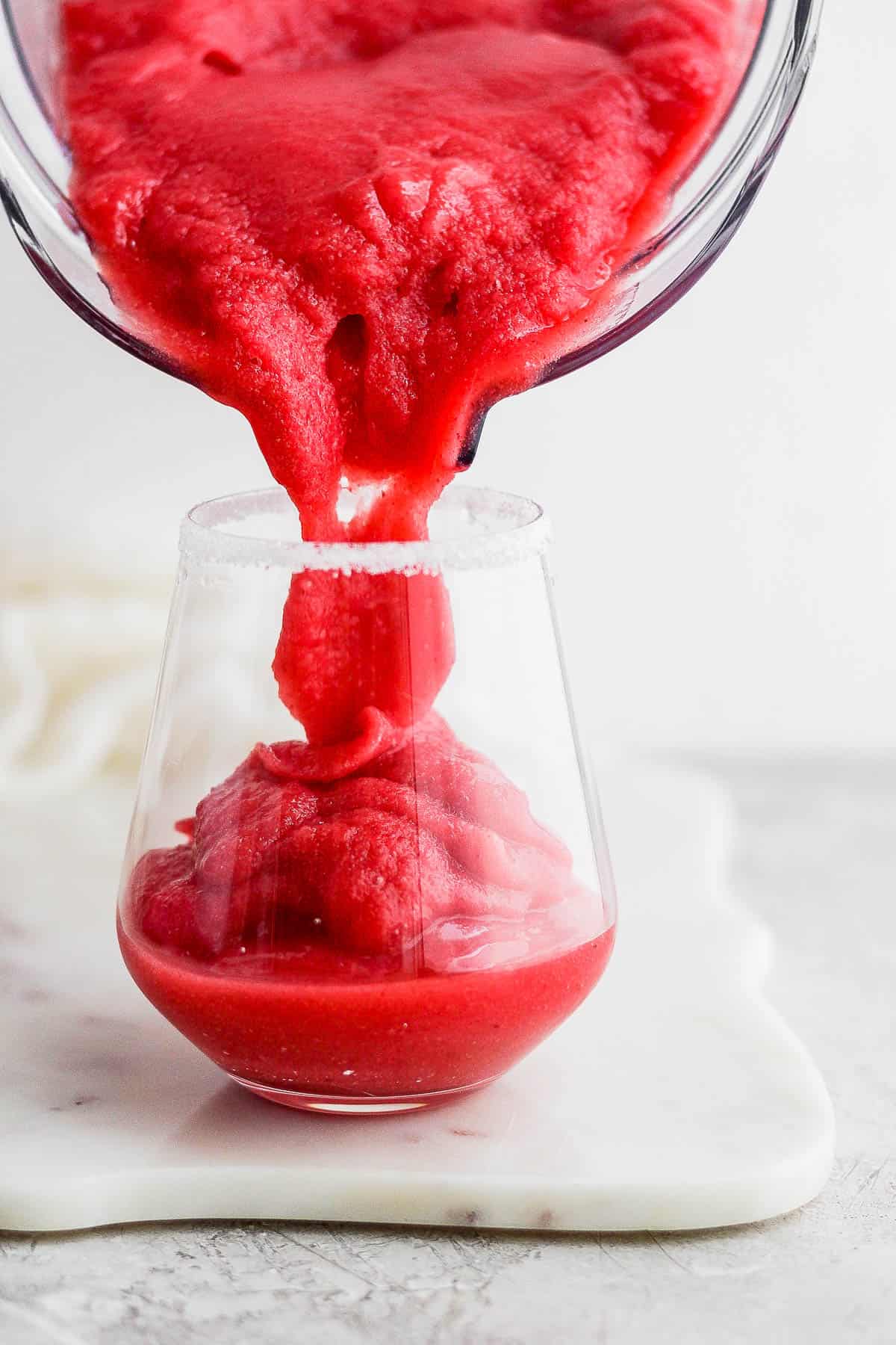 Frozen strawberry margaritas being poured into a glass.