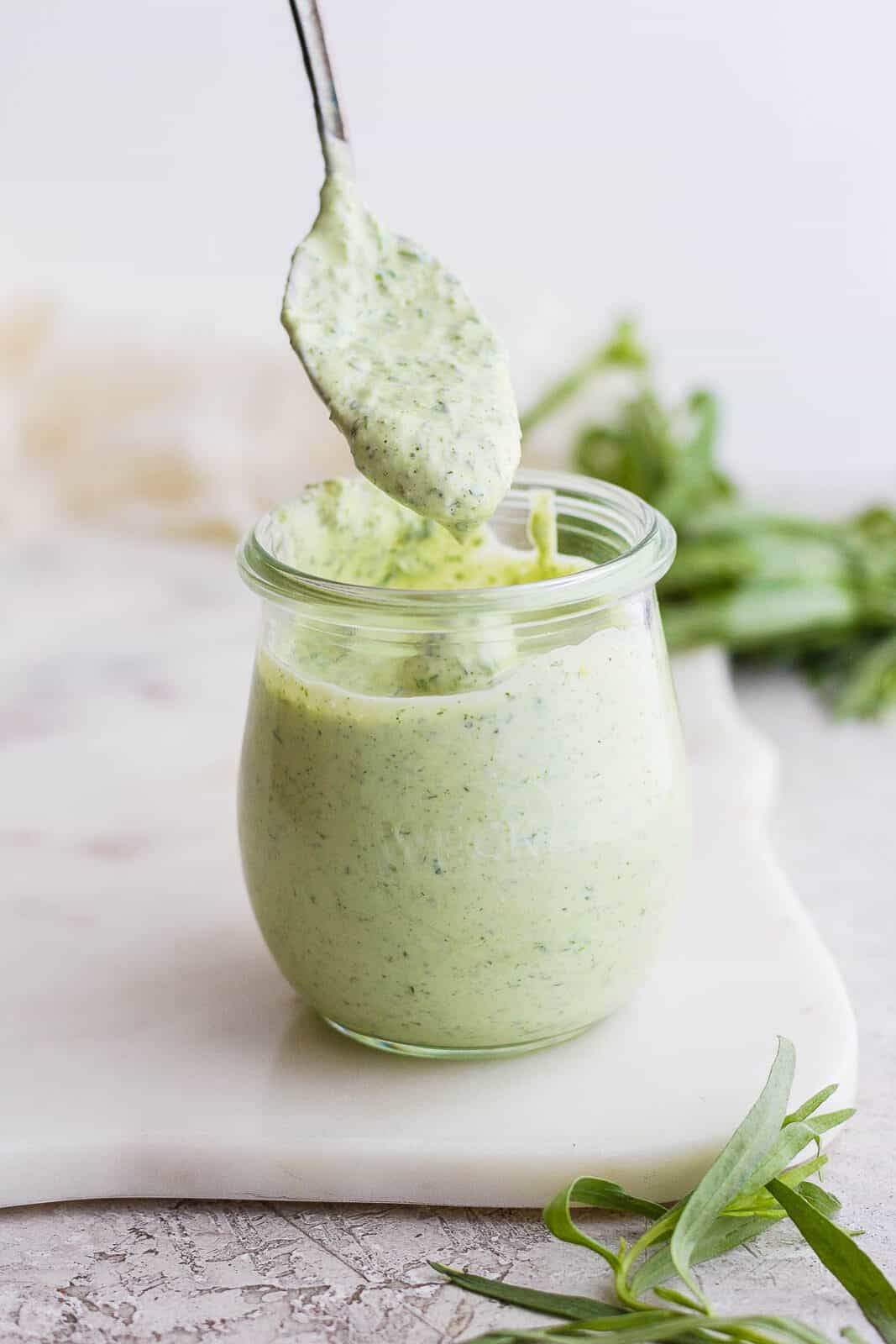 Green goddess dressing dripping off a spoon and into a jar.