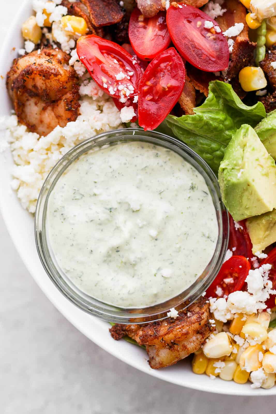 Homemade green goddess dressing in a dish with a grilled shrimp salad.