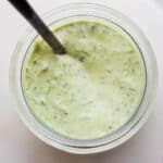Top shot of a small jar of green goddess dressing with spoon sticking out.