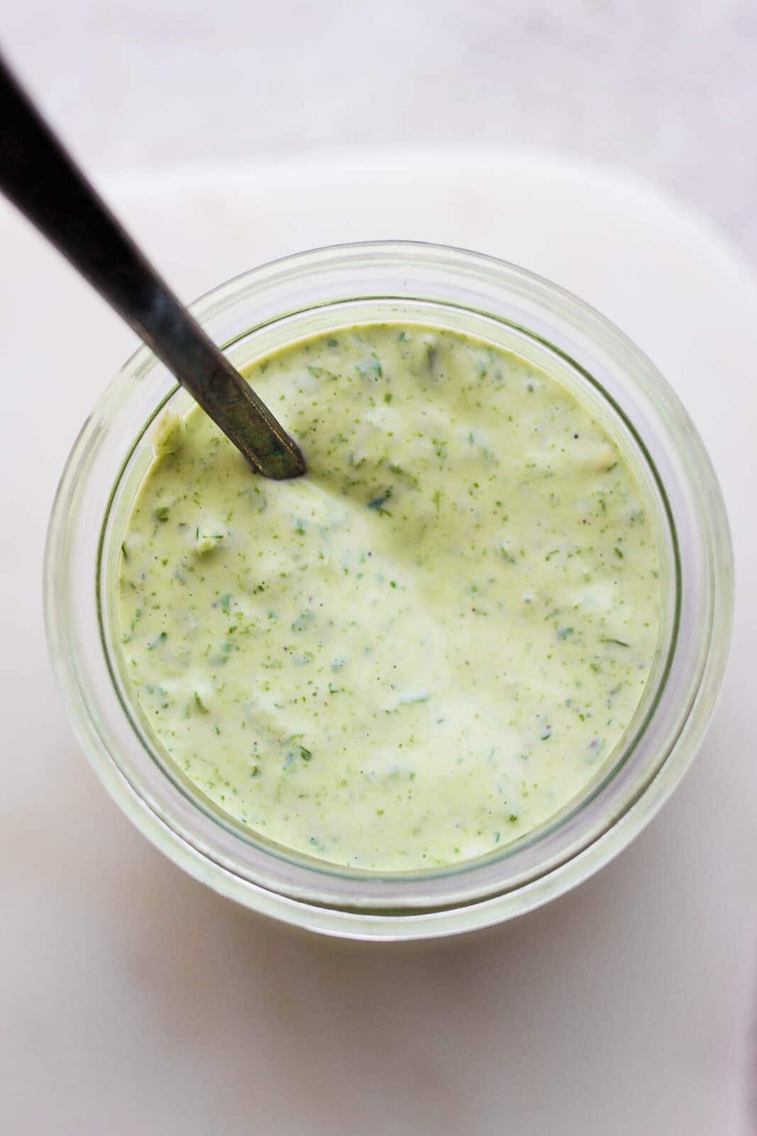 A jar of green goddess dressing with a spoon.