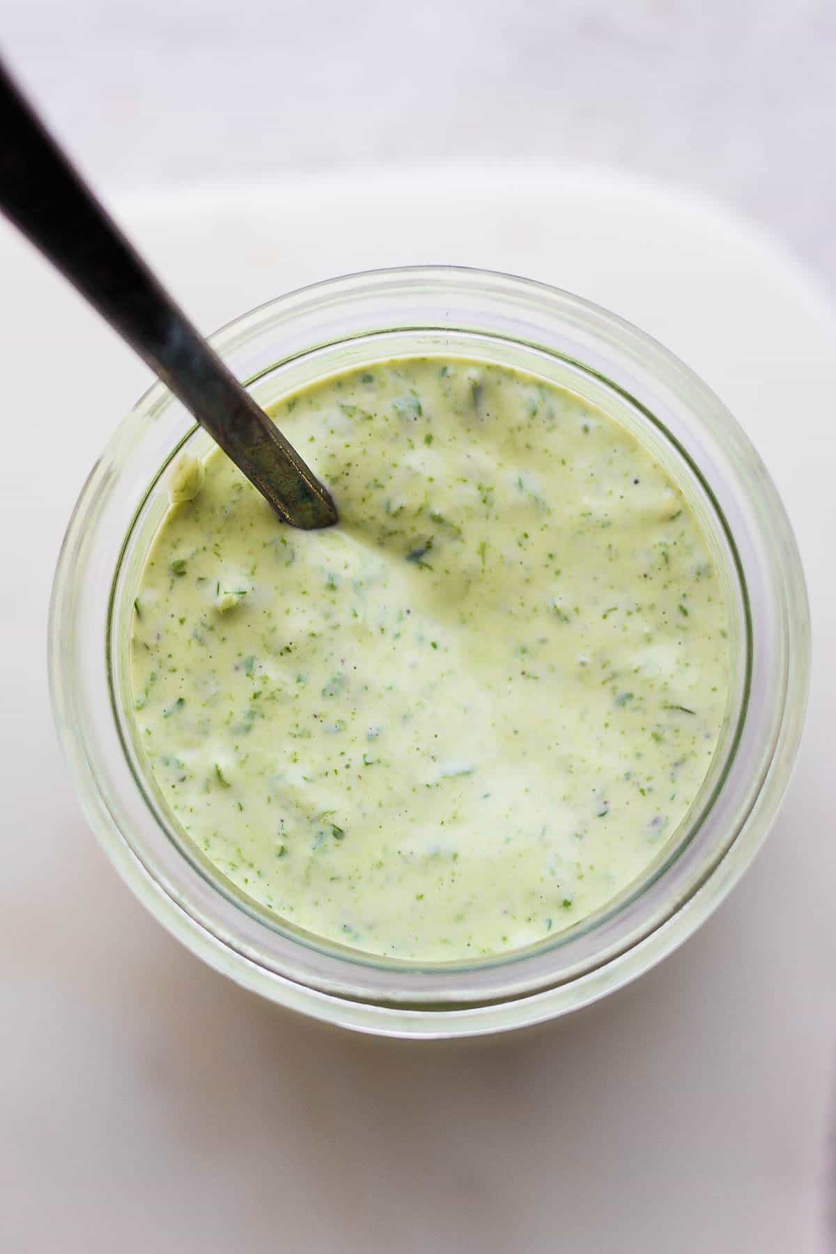 Green goddess dressing in a small glass container with a spoon.