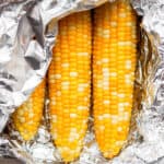 Three pieces of corn that are still in foil after being grilled.