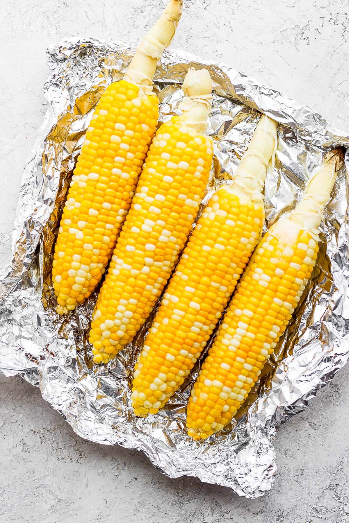 Four ears of cooked corn on the cob laying on top of a piece of foil. 