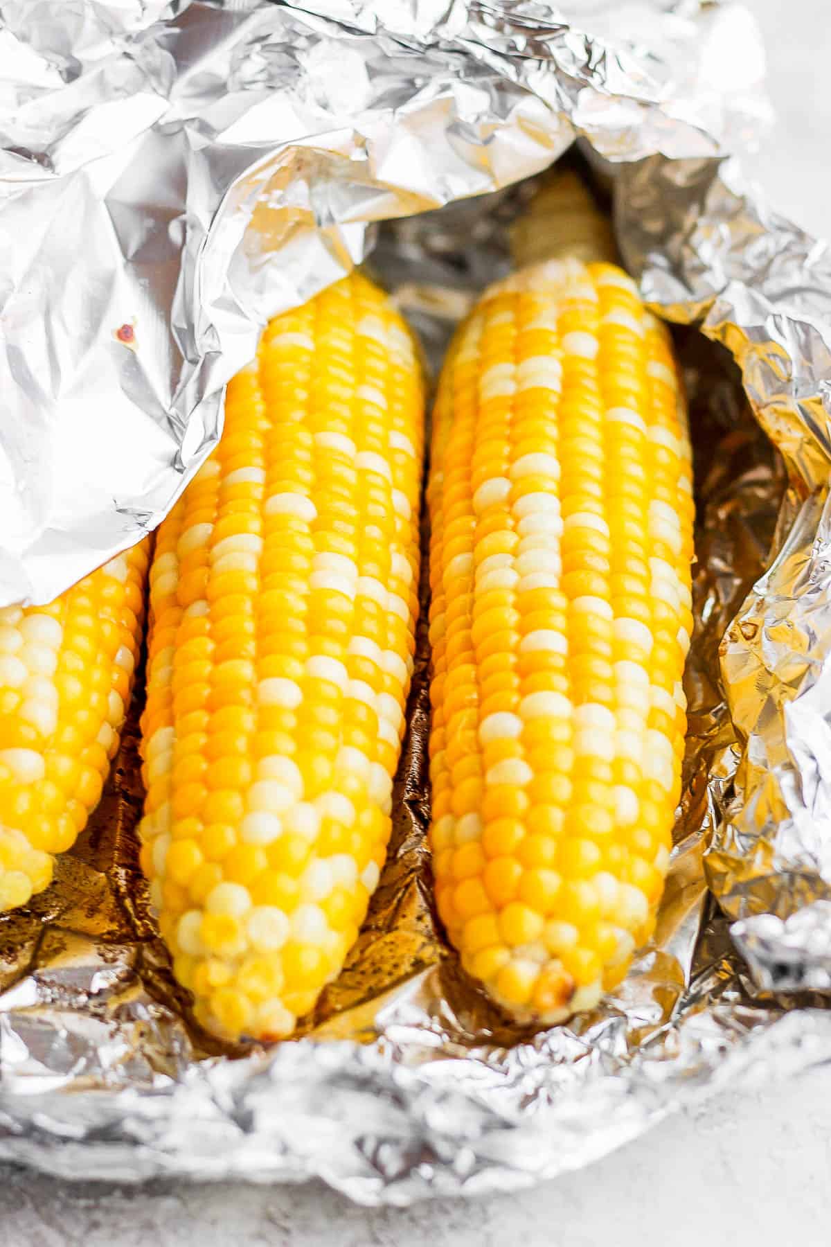Three ears of corn wrapped in a foil packet with one edge pulled back.