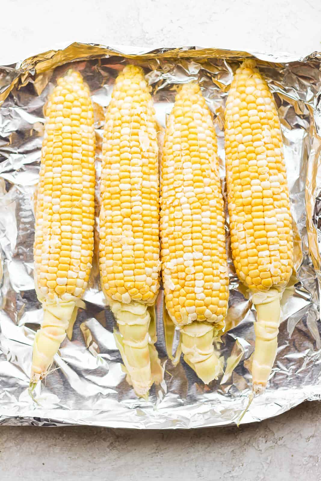Four ears of corn laying side by side on a piece of heavy duty foil. 