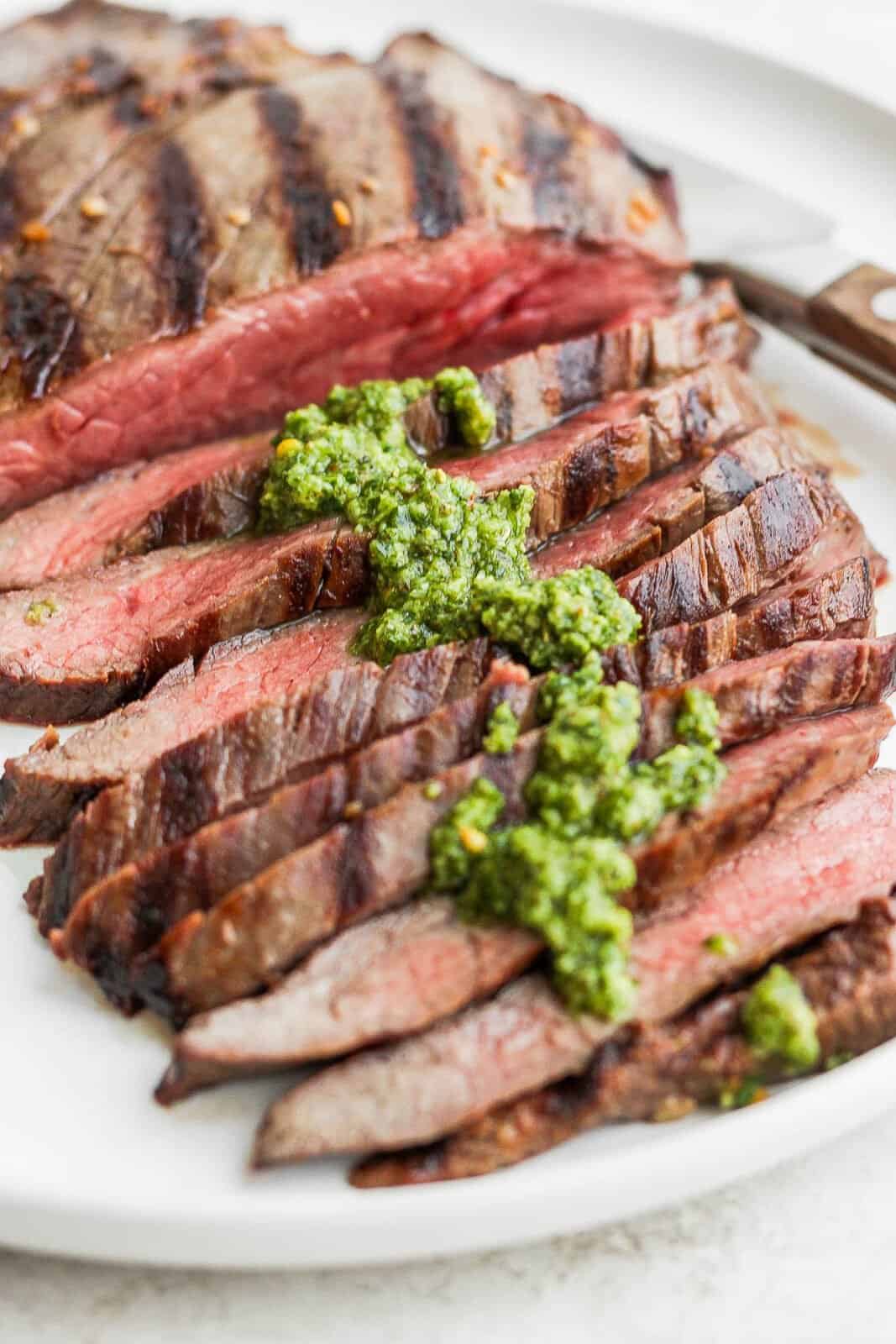 Side angle of a sliced piece of flank steak with chimichurri sauce on it. 