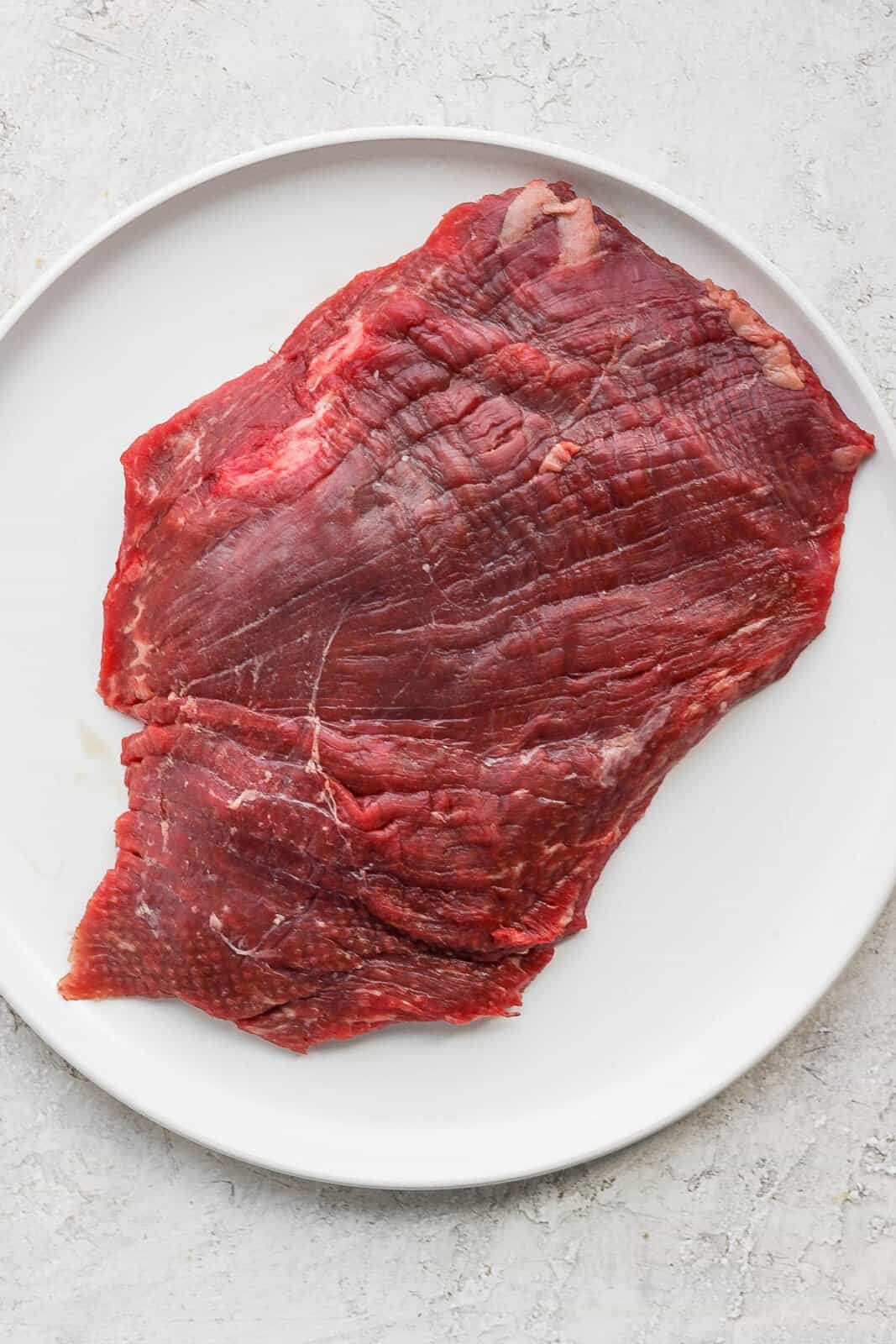 A raw flank steak on a plate.