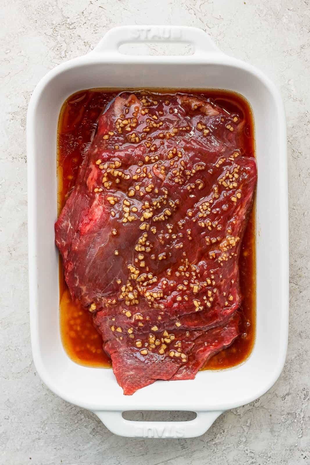 A flank steak sitting in a baking dish covered in a marinade.