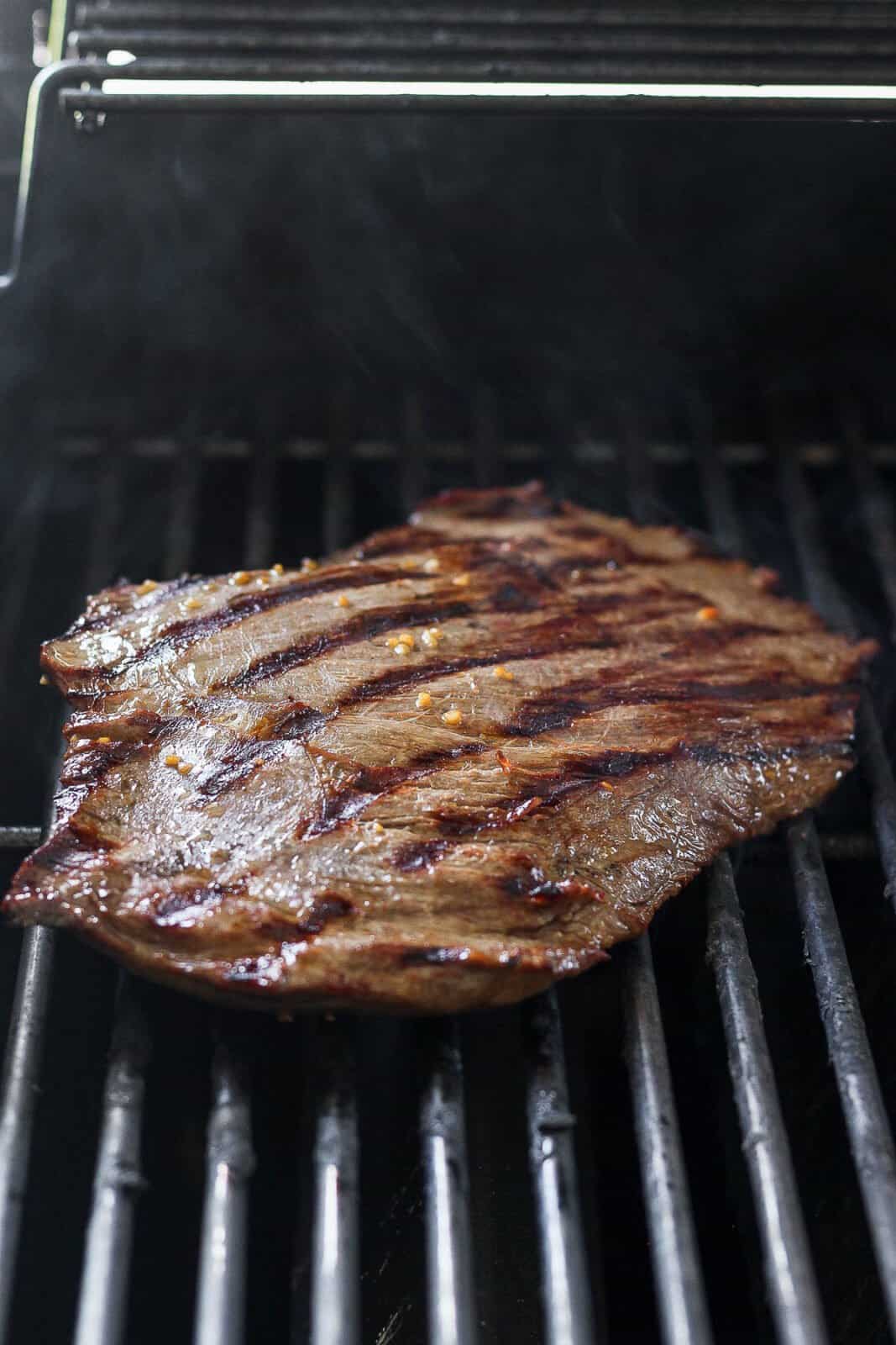 A flank steak cooking on the grill.