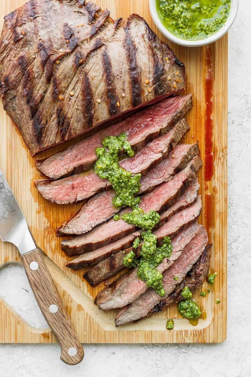Close up of a sliced piece of flank steak with chimichurri on it.