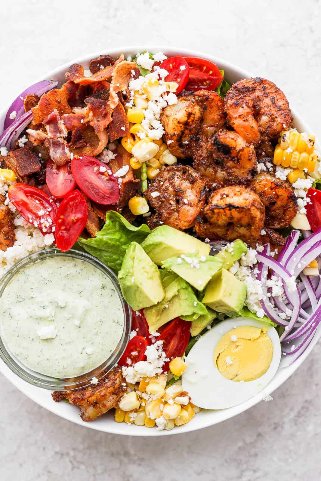 Blackened shrimp on a salad with a dish of green goddess dressing.