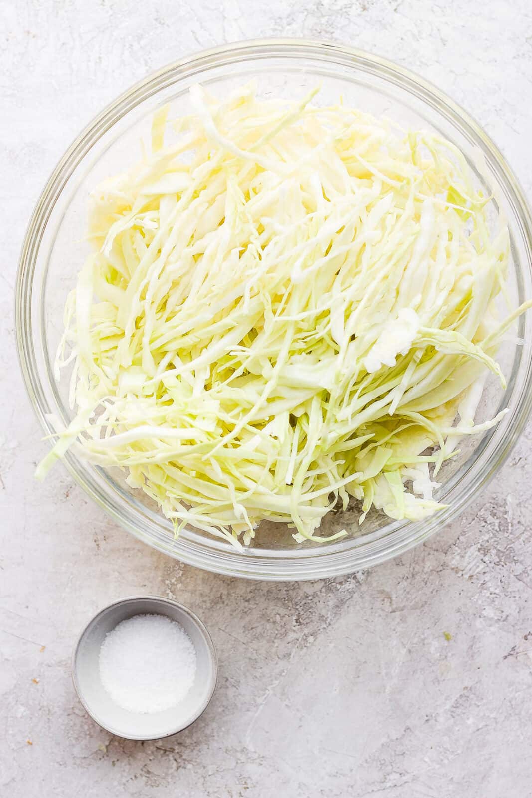 Thinly sliced cabbage in a large bowl and a small bowl of kosher salt.